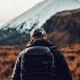 view of a man from behind walking towards a mountain with a backpack on