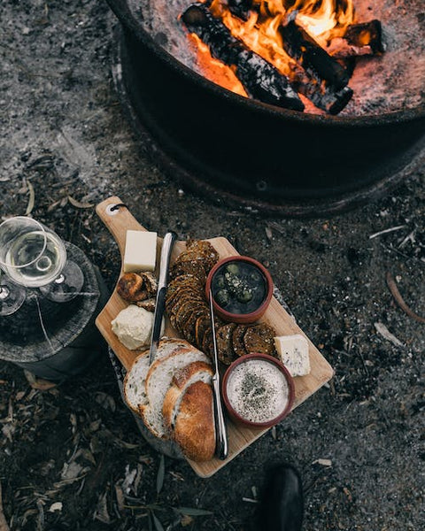 chefs board with bread and other food near an outdoor fire