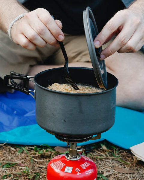person stirring noodles in a pot over a camping stove