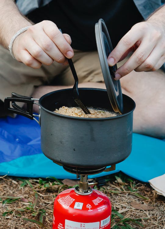 person stirring noodles in a pot over a camping stove